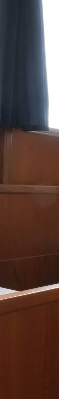 Een interieur van een boot met houten wanden, banken en een ronde tafel, met ramen met blauwe gordijnen.