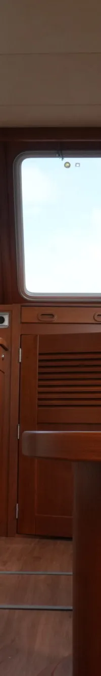 De foto toont het interieur van een boot met houten afwerking, ramen rondom, een tafel en zitplaatsen.