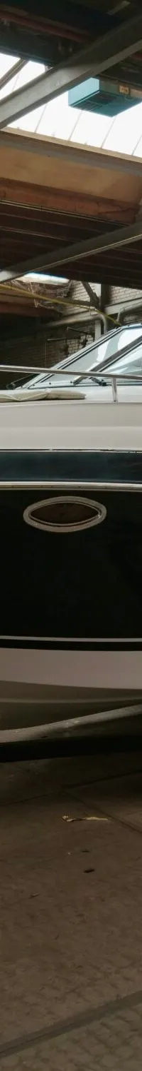 Een witte en donkerblauwe boot staat op een trailer in een loods met een Nederlands vlaggetje aan de boeg.