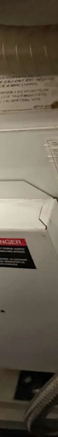 Een witte boiler met diverse aansluitingen en waarschuwingsstickers is zichtbaar.