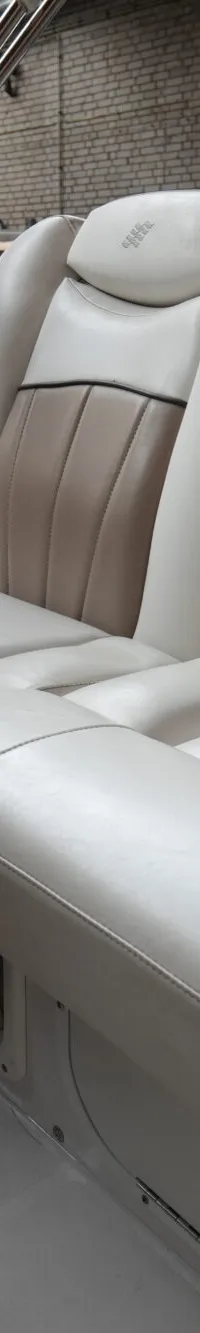 De foto toont het interieur van een boot met twee beige en witte stoelen, een stuur en een voorruit.