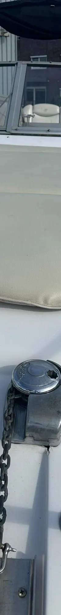 De foto toont het interieur van een bootkajuit met een ronde houten tafel, omringd door gestoffeerde zitbanken.