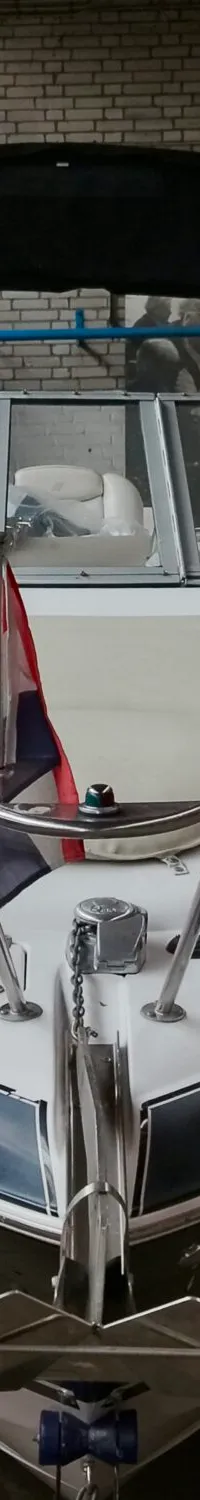 Een witte boot met een donkere streep en een Nederlandse vlag aan de boeg, staat in een loods.
