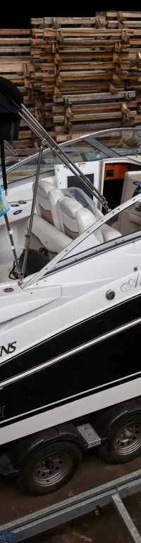 Een witte en zwarte boot met de naam "Angélique" en "FOUR WINNS" op de zijkant, staat op een trailer.