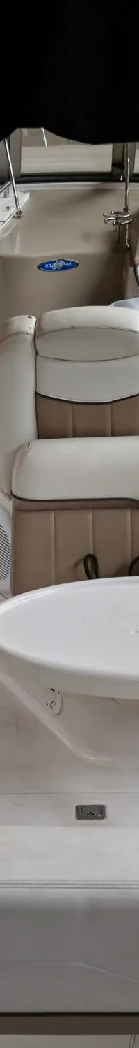 De foto toont het interieur van een boot met beige en witte bekleding, een stuur, meters en een tafel.