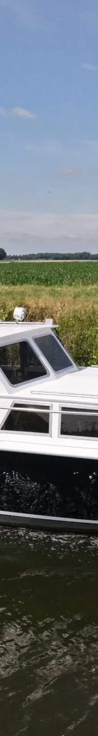 Een donkerblauwe met witte motorboot vaart op een waterweg langs groene velden onder een blauwe lucht.