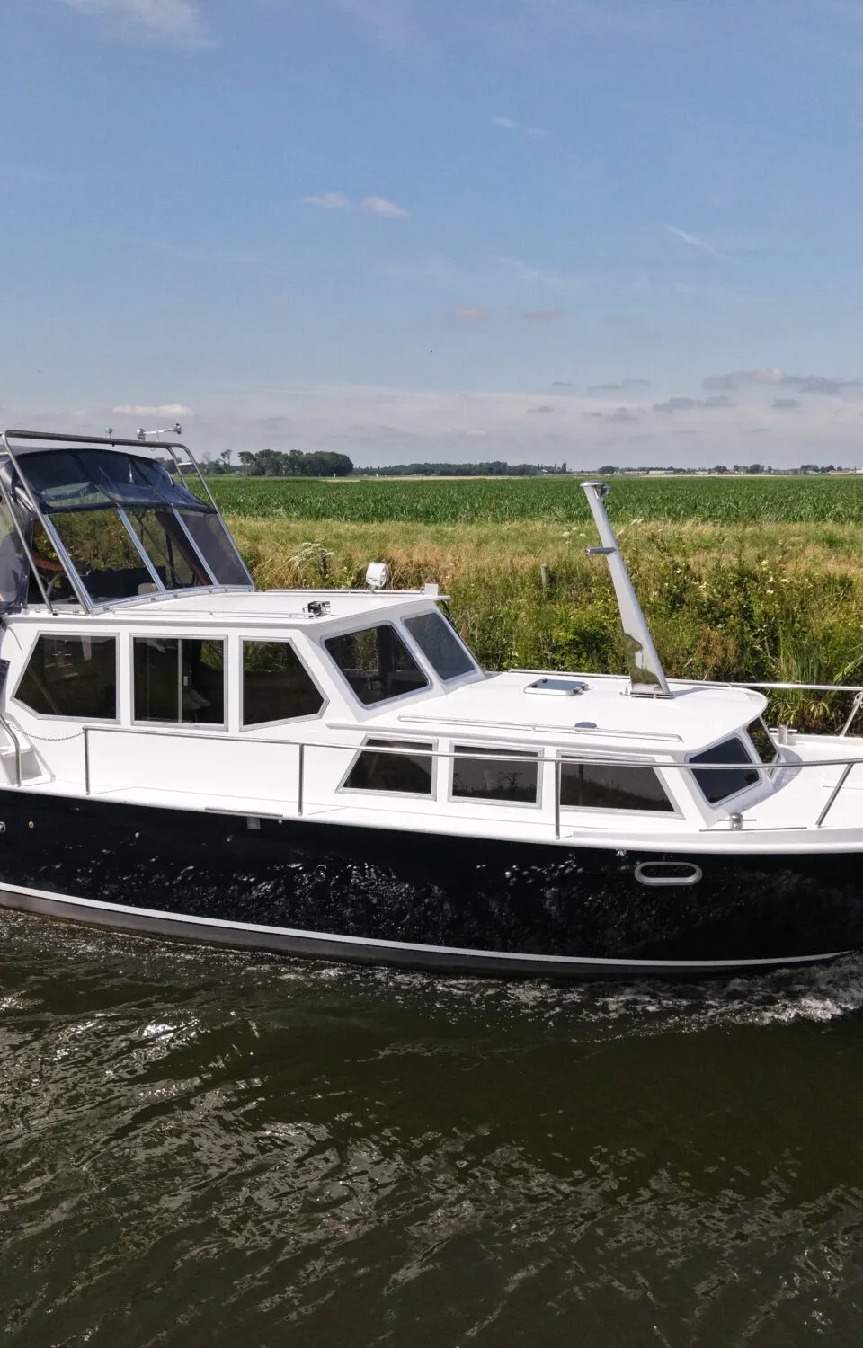 Een donkerblauwe met witte motorboot vaart op een waterweg langs groene velden onder een blauwe lucht.