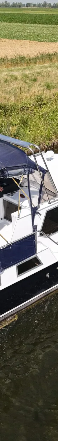 Een witte motorboot met donkerblauwe romp en kap vaart op een kanaal langs groene en gele velden.