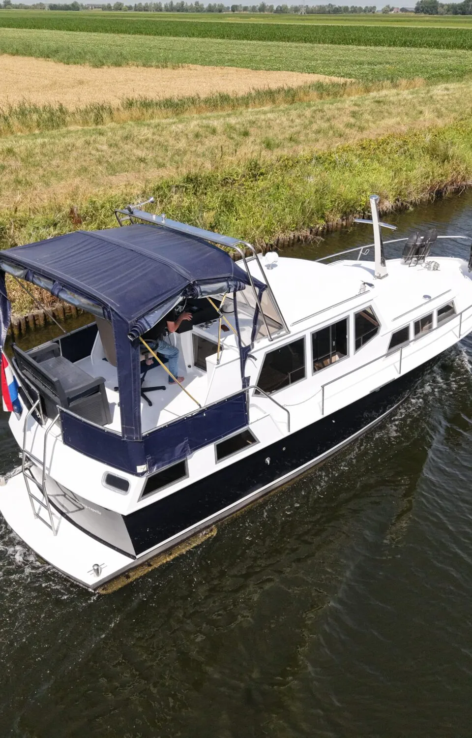 Een witte motorboot met donkerblauwe romp en kap vaart op een kanaal langs groene en gele velden.