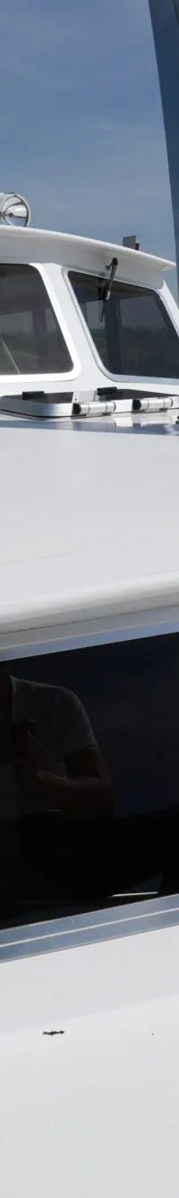 De foto toont de witte boeg en opbouw van een boot met ramen en een stalen mast, varend op een kanaal.