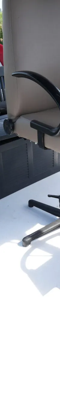 Op het witte achterdek van een boot staan een beige draaistoel, een donkere bank met opbergruimte en een wit stuurwiel.