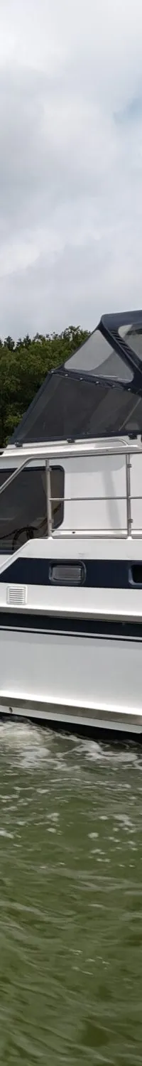 Een witte motorboot met donkerblauwe accenten vaart op een waterweg, met een Belgische vlag aan de achtersteven.