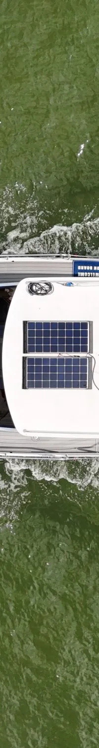 Een dronefoto van bovenaf toont een witte motorboot met een grijs dek, zonnepanelen en een donkerblauwe bimini.