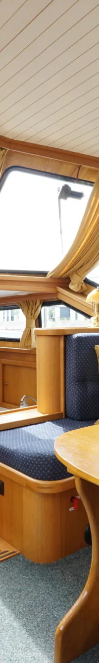 De foto toont het interieur van een boot met een stuurwiel, houten afwerking, blauwe banken en een tafel.
