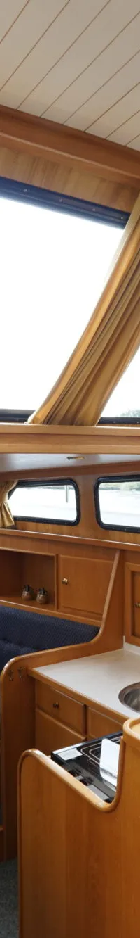 De foto toont het interieur van een boot met een houten stuurwiel, blauwe zitbanken en een kleine keuken.
