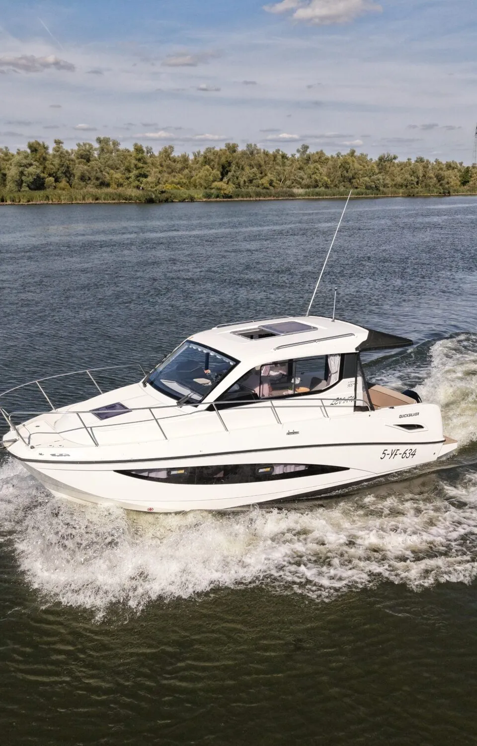 Een witte motorboot met registratienummer 5-VF-634 vaart op het water, met een persoon aan boord en bomen op de achtergrond.
