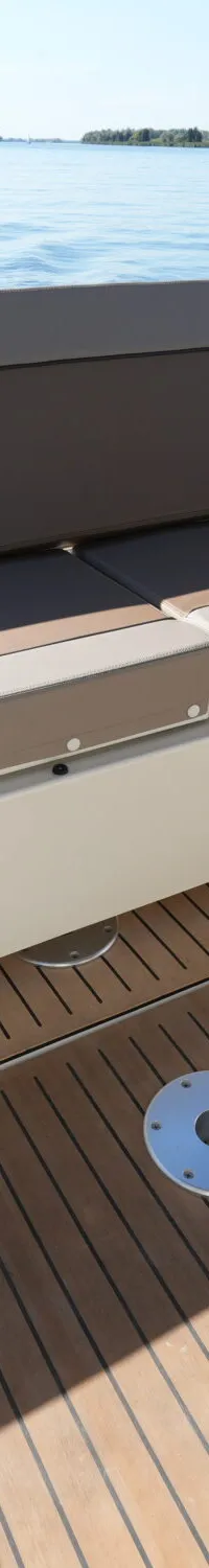 De achterkuip van een boot met beige en bruine kussens, een teak-look vloer en uitzicht op water met andere boten.