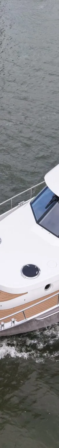 Een wit met grijs motorjacht vaart op het water, met een bruin dek, stootwillen aan de boeg en een open dak.