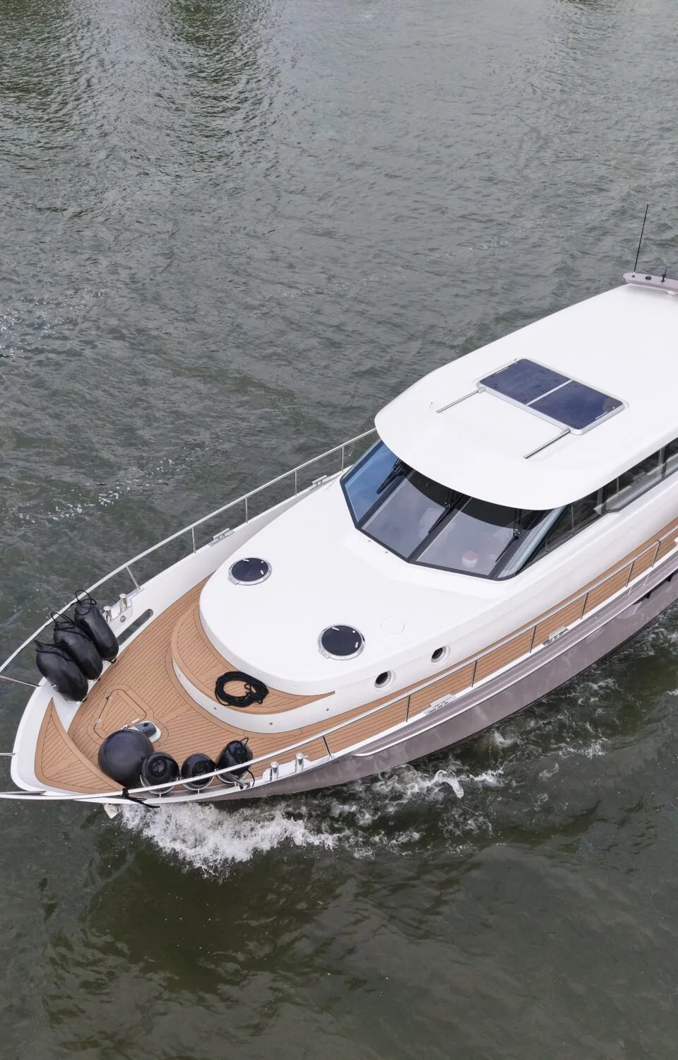 Een wit met grijs motorjacht vaart op het water, met een bruin dek, stootwillen aan de boeg en een open dak.