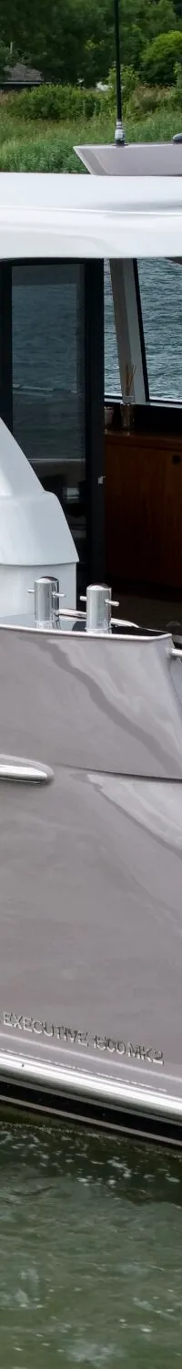Een grijs-witte motorjacht met de naam "SERVUS" en "ZWIJNDRECHT" vaart op het water met een Nederlandse vlag.