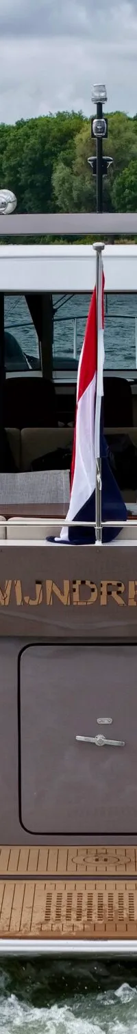 De achterkant van een motorjacht met de naam "ZWIJNDRECHT" is zichtbaar, met een Nederlandse vlag en een teakdek.