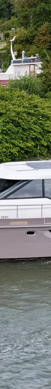 Een lichtbruine motorjacht met witte opbouw en de naam "SERVUS" op de spiegel vaart op het water met een Nederlandse vlag.