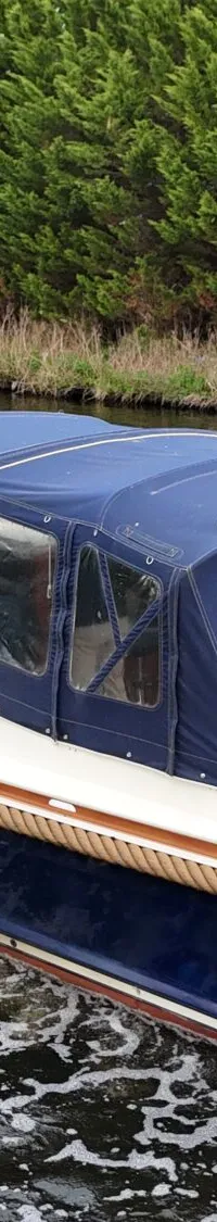 Een blauw-witte motorboot met een blauwe kap vaart over een waterweg met een vlag aan de achtersteven.