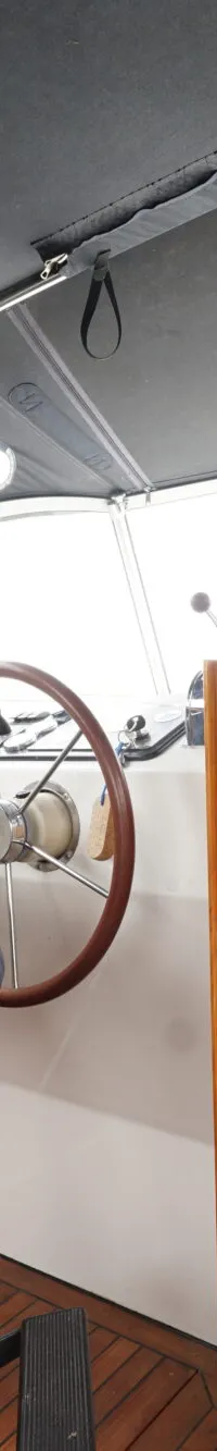 Een blauwe stuurstoel met armleuningen en een houten stuurwiel zijn zichtbaar in de cockpit van een boot.