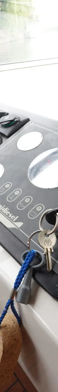 Een close-up van het stuur en het dashboard van een boot, met een blik op het water en de oever door de ramen.