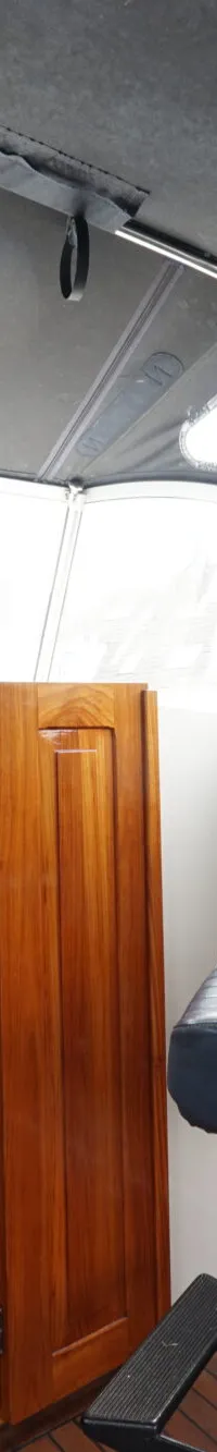 De foto toont het interieur van een boot met een stuurstand, een open kajuitingang en een blauwe stuurstoel.