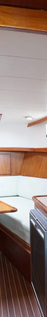 De foto toont een interieur van een boot met houten afwerking, een zithoek, een tafel en een keukenblok met twee spoelbakken.