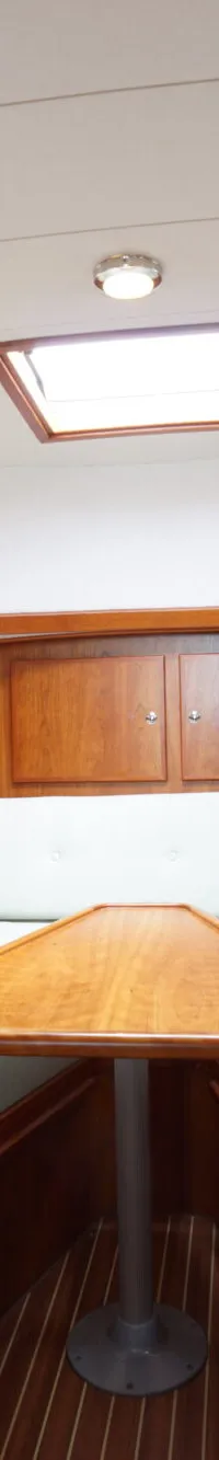 De foto toont een kajuit met houten wanden, witte kussens, een houten tafel en een dakraam.