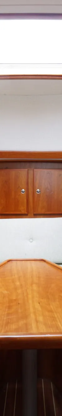 Een kajuit met houten wanden, lichte kussens, een houten tafel, twee patrijspoorten en een dakluik.