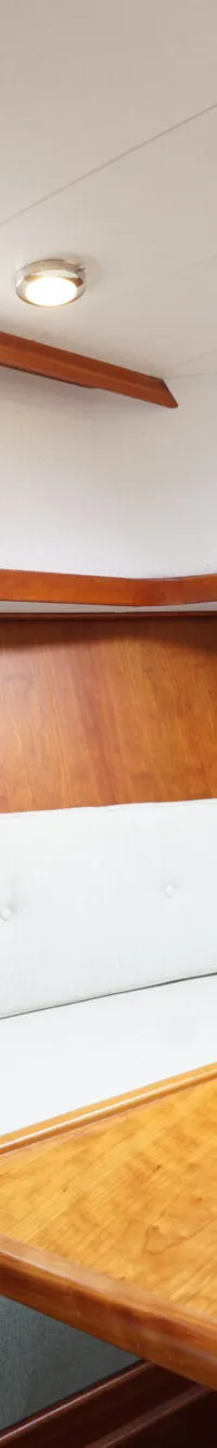 Een interieur van een boot met houten wanden, een lichte bank, een houten tafel en twee patrijspoorten.