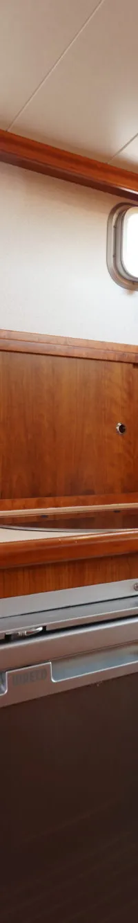 Een kombuis met houten kasten, een gootsteen, een kraan, een koelkast en twee patrijspoorten.