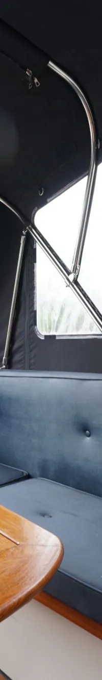 Een interieur van een boot met een houten tafel, blauwe banken en uitzicht op water en bomen.