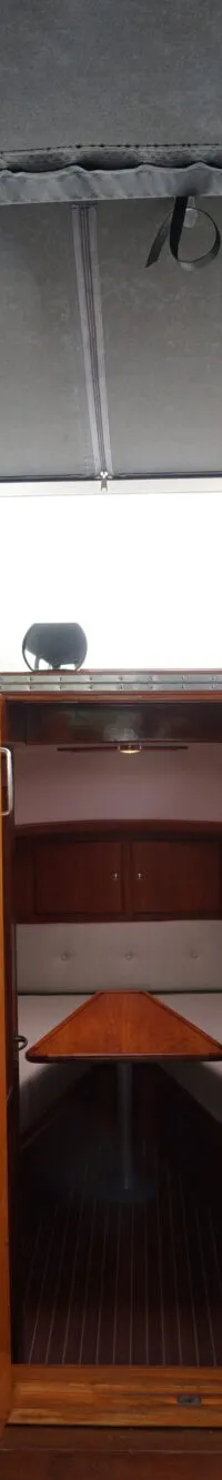 De foto toont het interieur van een boot met een stuurwiel, twee blauwe stoelen en een doorgang naar een kajuit.