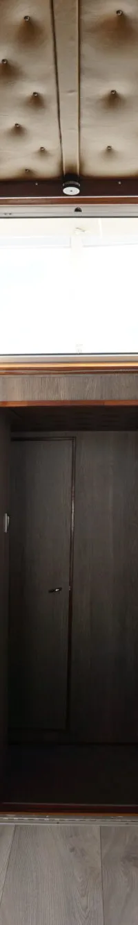 De foto toont het interieur van een boot met een stuurstand, zitplaatsen, ramen met gordijnen en een gestoffeerd plafond.