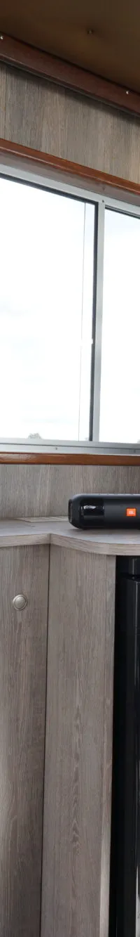 De foto toont het interieur van een boot met een stuurstand, een stuurstoel, ramen met gordijnen en een ingebouwde koelkast.