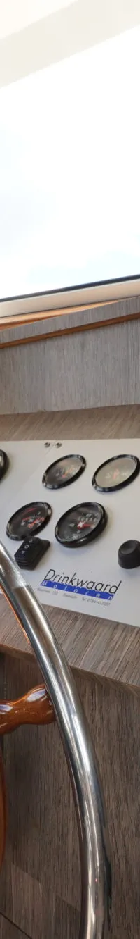De foto toont het stuurhuis van een boot met een houten stuurwiel, diverse meters, een navigatiescherm en een gashendel.