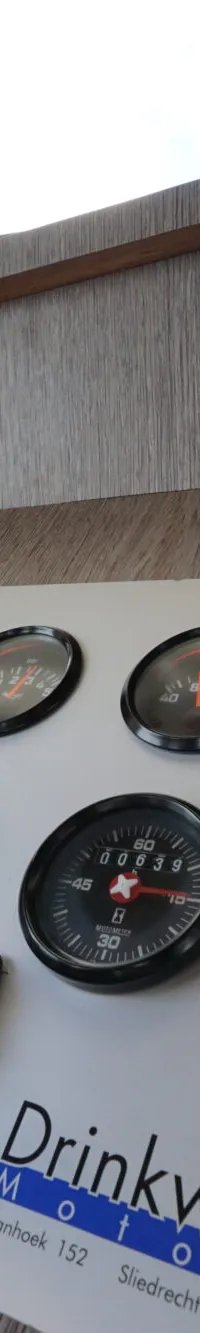 Een stuurstand met diverse meters, een monitor en een stuurwiel, met op de achtergrond een raam met gordijnen.