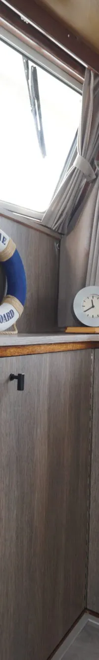 De foto toont een interieur van een boot met houten wanden, ramen met gordijnen, en decoratieve items zoals een…