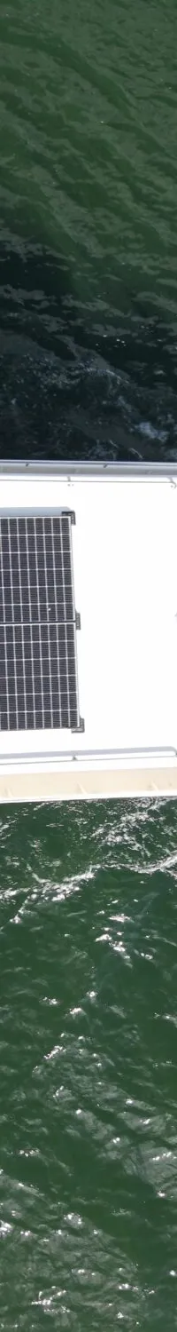 Een witte boot met een Nederlandse vlag aan de achtersteven en zonnepanelen op het dak vaart over groen water.
