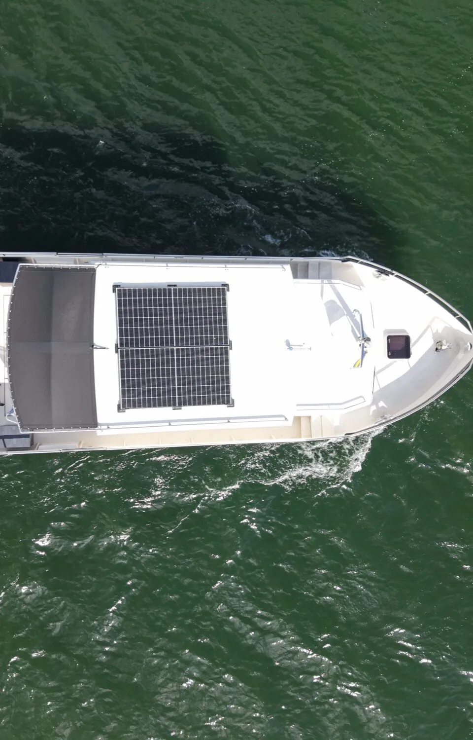Een witte boot met een Nederlandse vlag aan de achtersteven en zonnepanelen op het dak vaart over groen water.