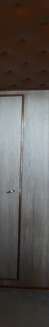 Een gang met houten wanden en een bruin, gewatteerd plafond, met twee deuren aan het einde en een aan de rechterkant.