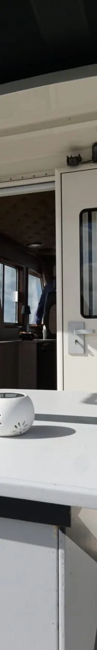 Een witte boot met een tafel en stoelen op het dek, met uitzicht op water en een beboste oever.