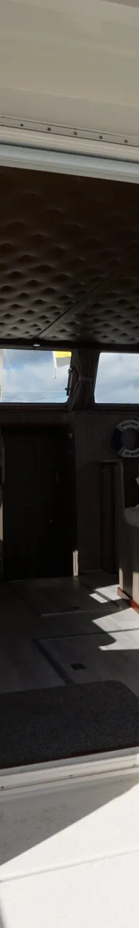 Een open schuifdeur van een boot toont een stuurhut met een persoon aan het roer en een reddingsboei.