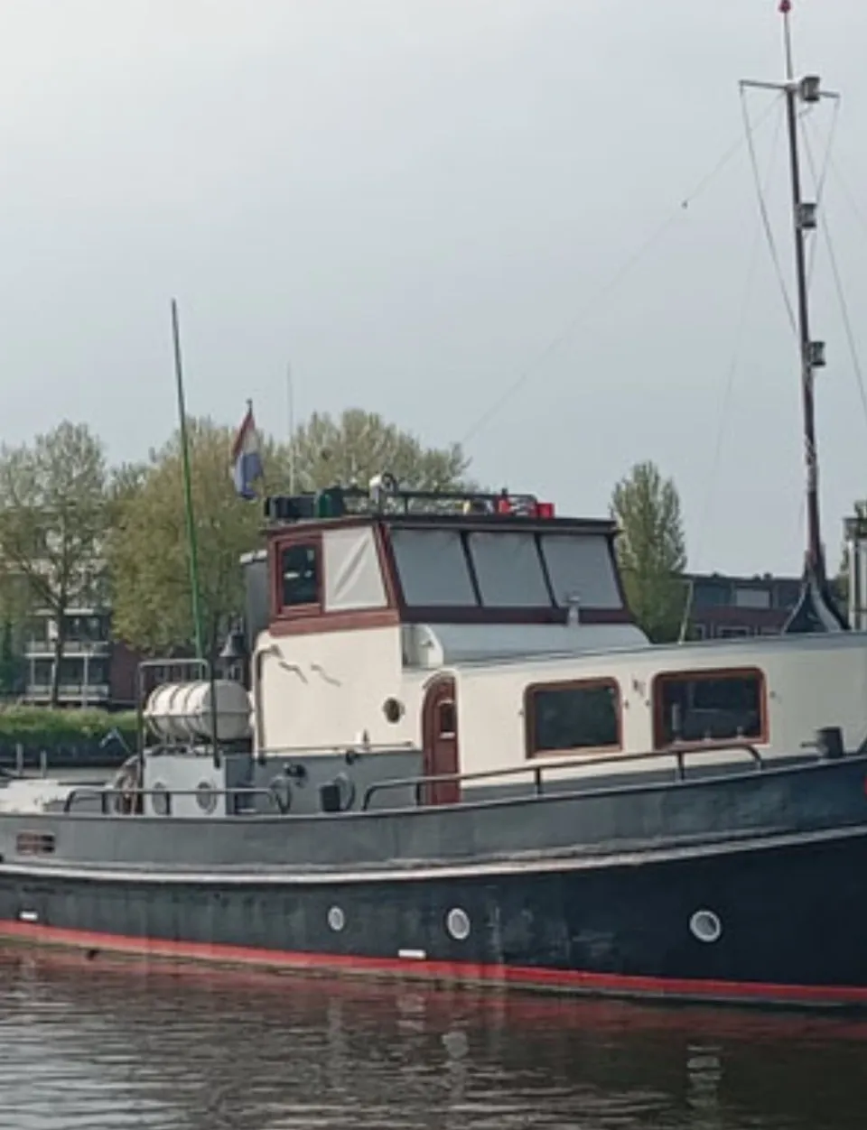 Een donkerblauwe boot met een witte opbouw en rode accenten ligt in het water, met "JAN ABELS" op de boeg.
