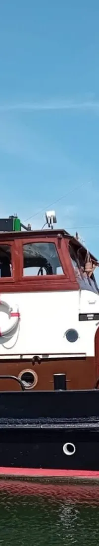 Een zwarte boot met een rode waterlijn en witte opbouw, met de naam "JAN ABELS" op de boeg en een Nederlandse vlag achterop.