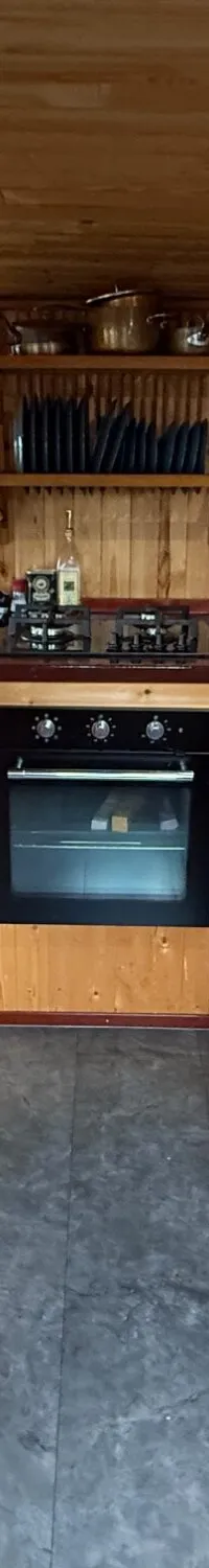 Een houten kombuis met een U-vormig aanrecht, een gasfornuis, oven, koelkast en diverse keukengerei.